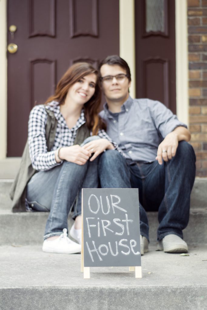 couple sitting on new home steps with our first house sign in front